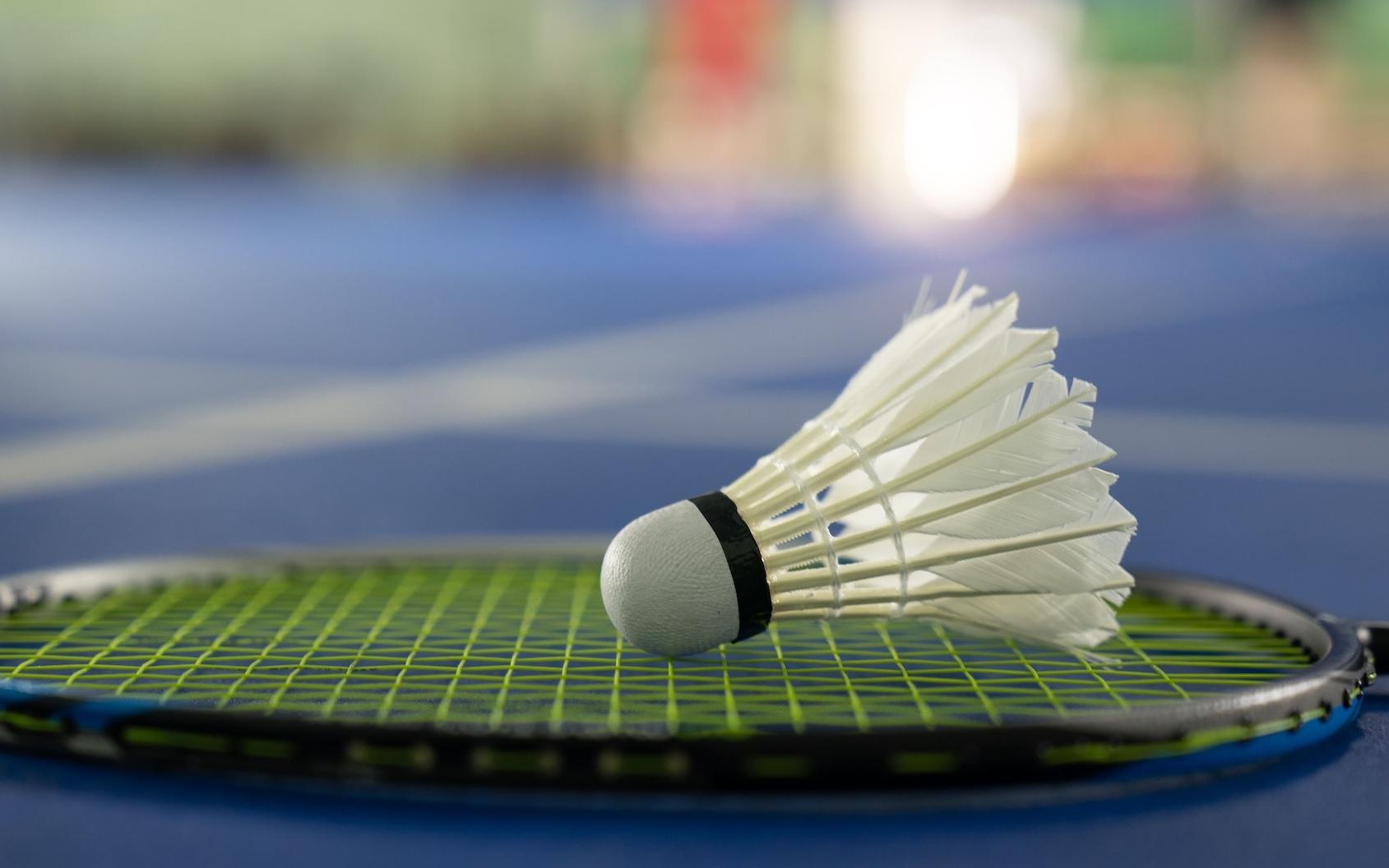 Nahaufnahme eines Federballs auf einem Badmintonschläger, ruhend auf einem blauen Badmintonplatz.