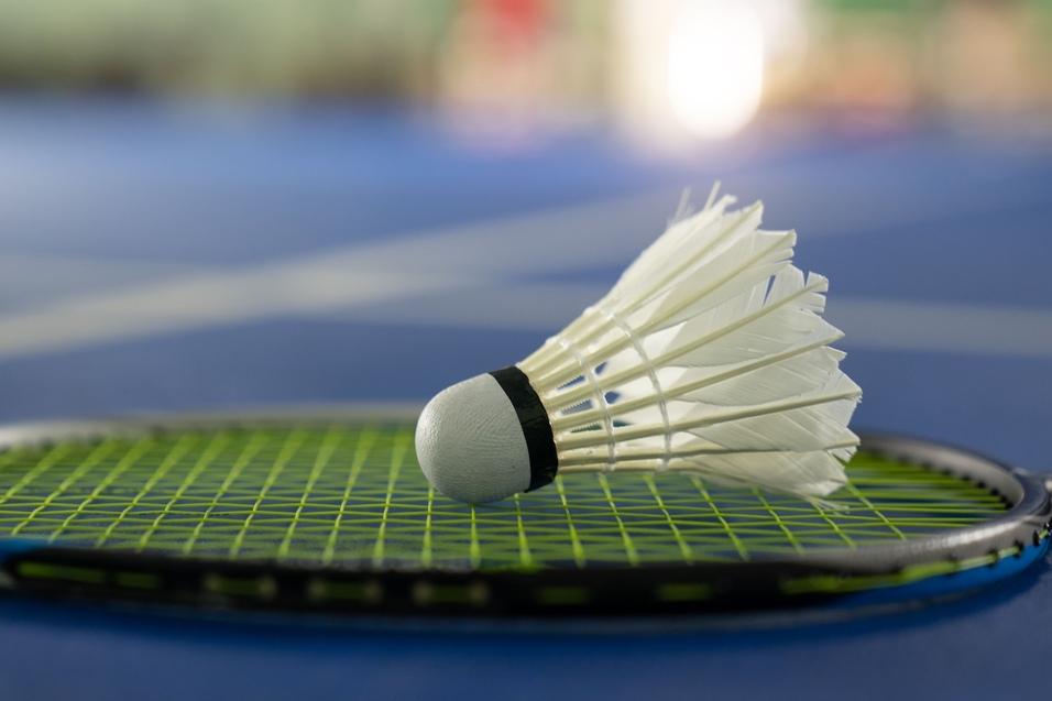 Nahaufnahme eines Federballs auf einem Badmintonschläger, ruhend auf einem blauen Badmintonplatz.