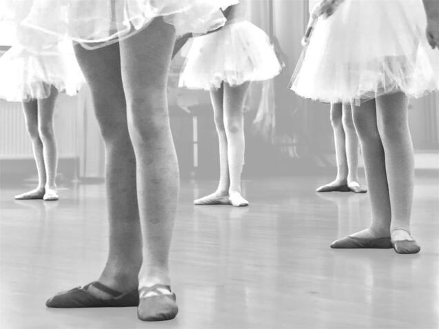 Beine von Balletttänzerinnen in Tüllröcken stehen auf einem Holzfußboden während des Trainings.