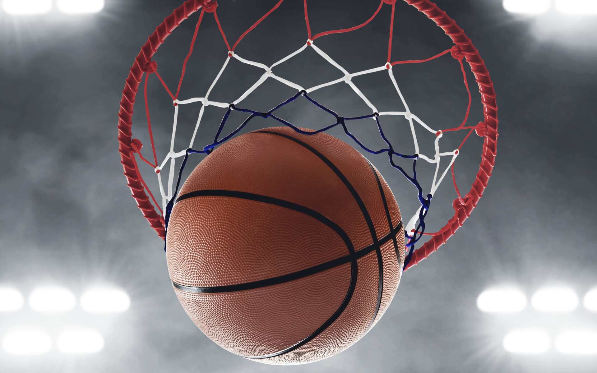 Nahaufnahme eines Basketballs, der durch den Basketballkorb in einem beleuchteten Sportumfeld fliegt.