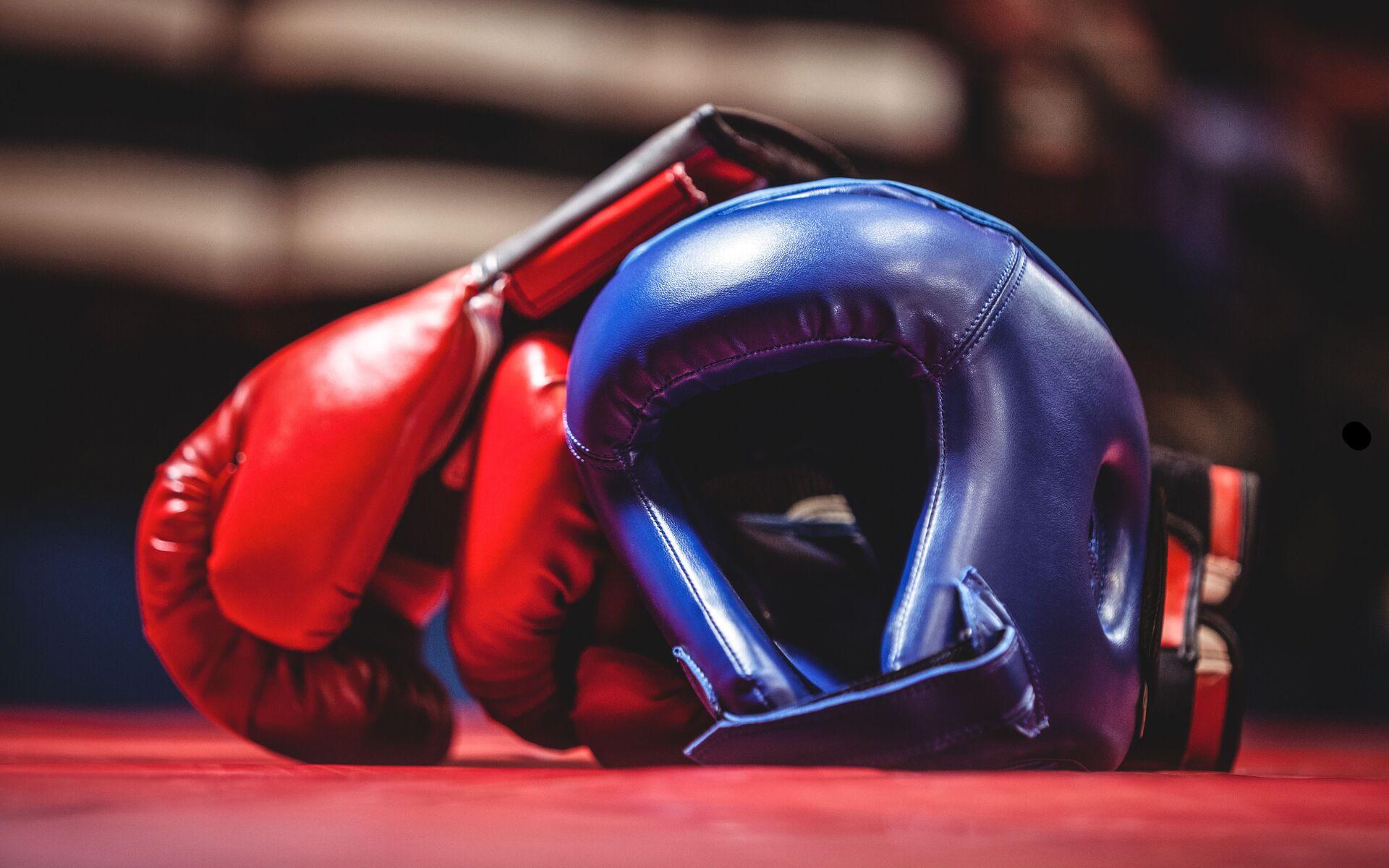 Rote Boxhandschuhe liegen neben einem blauen Kopfschutz auf einem roten Boxring.