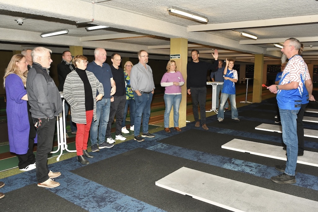 Gruppenteilnehmer lauschen einem Referenten auf einer sportlichen Veranstaltung in einer Halle mit Teppichboden.