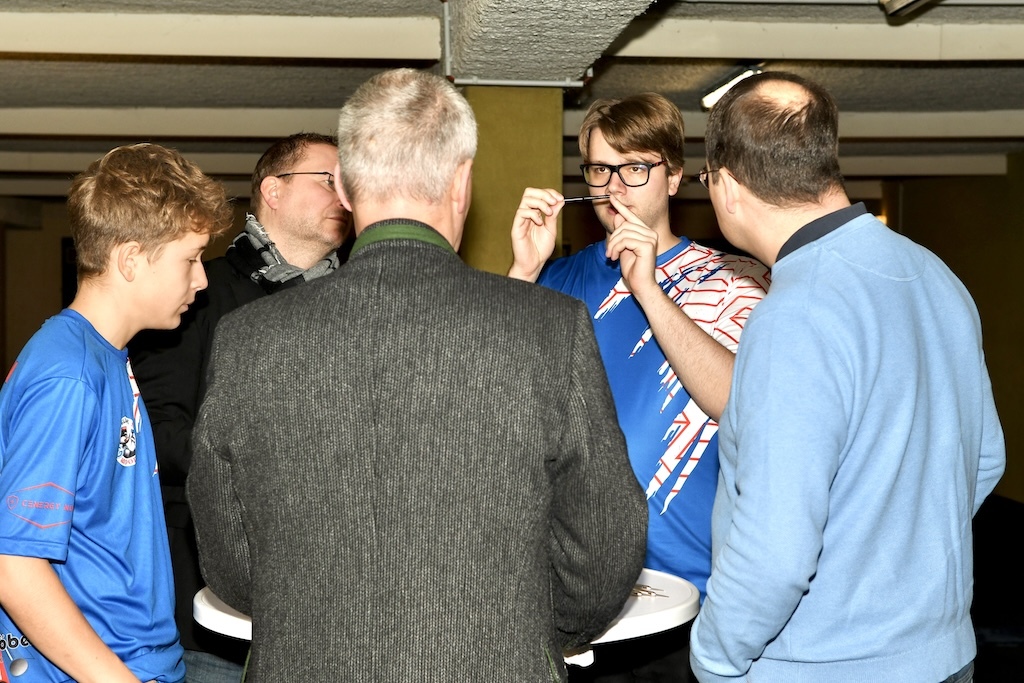 Gruppe von Menschen diskutiert an einem Stehtisch, w&auml;hrend ein junger Mann mit Brille gestikuliert.
