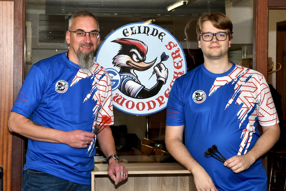 Zwei M&auml;nner in blauen Sporttrikots stehen vor einem Logo mit dem Schriftzug &bdquo;Glinde Woodpockers&ldquo;.