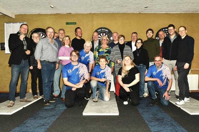 Gruppenscreenshot von 18 Personen in einem Dartsalon, einige tragen Dartshirts, Hintergrund mit Dartscheiben.