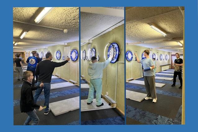 Gruppenszenen in einer Darts-Anlage mit Spielern, die auf verschiedene Dartboards konzentriert werfen.