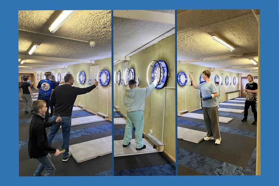 Gruppenszenen in einer Darts-Anlage mit Spielern, die auf verschiedene Dartboards konzentriert werfen.