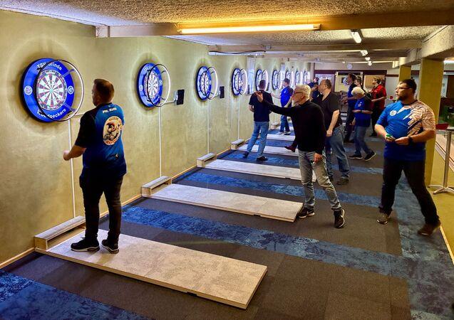 Gruppe von Dartspielern, die an mit Targets ausgestattet Wänden in einem Spielraum spielen.