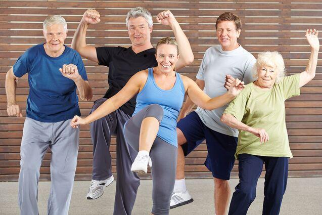 Gruppe von fünf älteren Menschen macht im Fitnessraum synchron Übungen zu Musik.