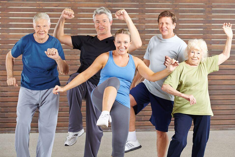 Gruppe von fünf älteren Menschen macht im Fitnessraum synchron Übungen zu Musik.
