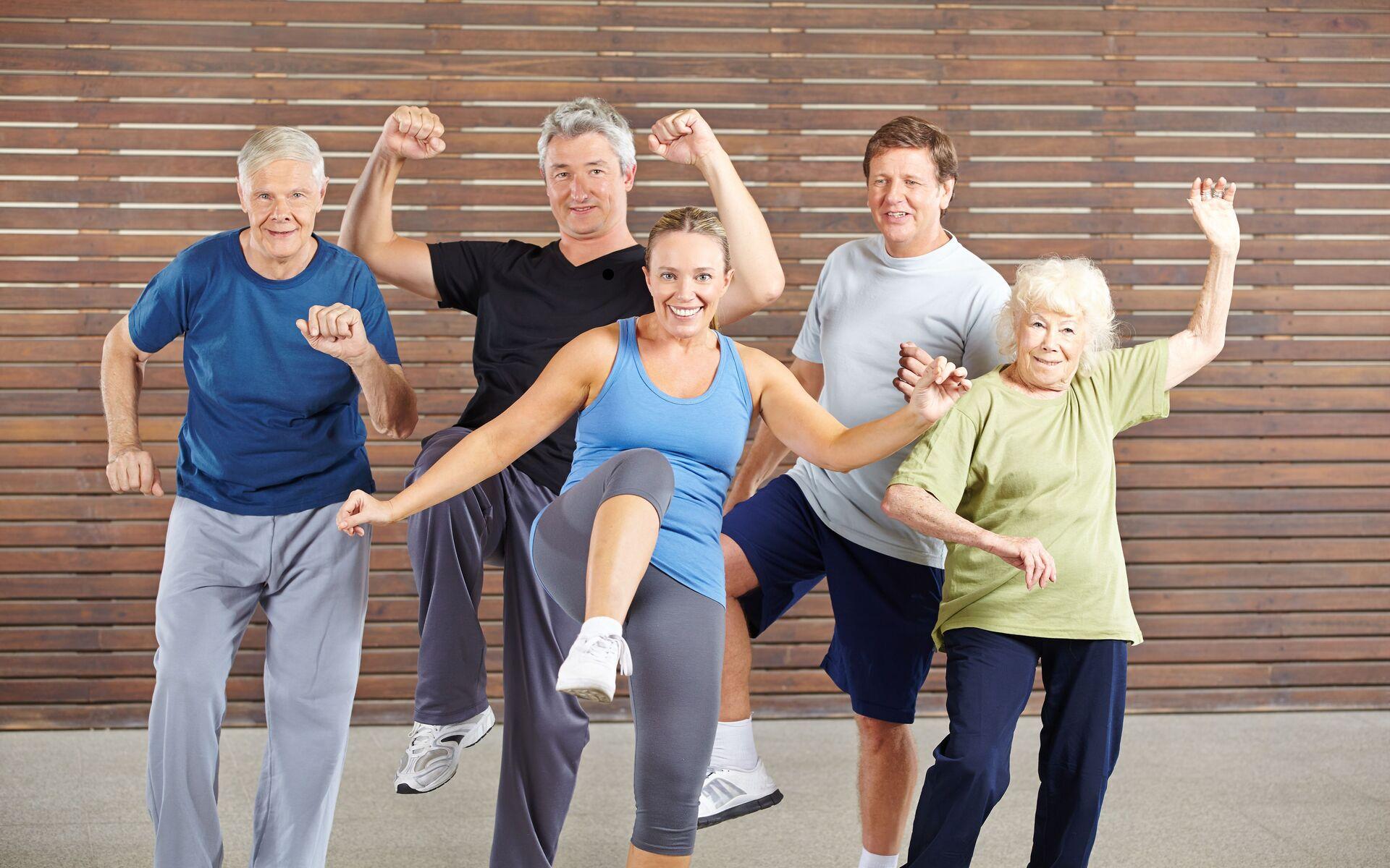 Gruppe von fünf älteren Menschen macht im Fitnessraum synchron Übungen zu Musik.