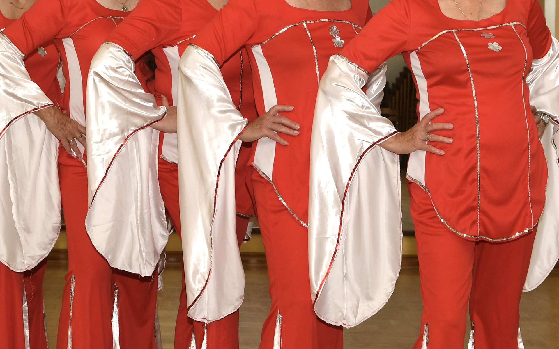 Gruppe von acht Damen in roten Kost&uuml;men mit wei&szlig;en &Auml;rmeln posiert in einem Tanzsaal.