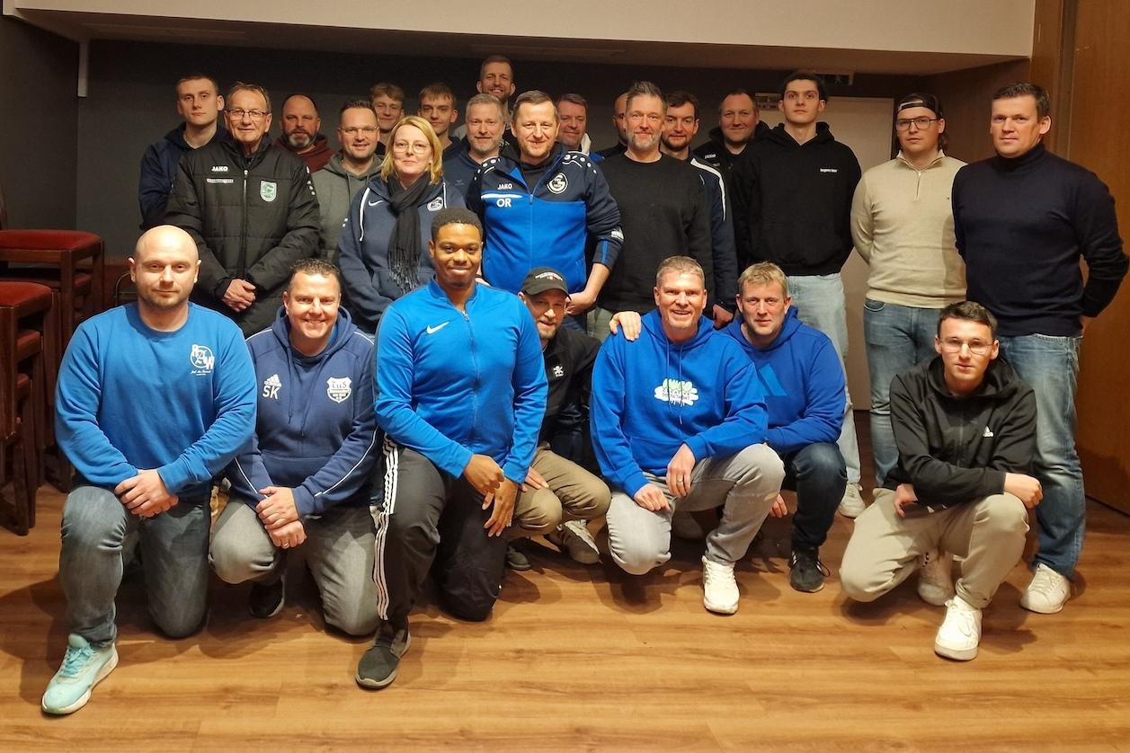 Gruppenfoto von Sportvereinsmitgliedern in blauen und schwarzen Outfits, auf einem Holzfußboden zusammengestellt.