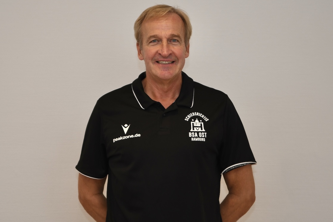 L&auml;chelnder Mann in dunklem Polo-Shirt mit Logo der BSA Ost Bamberg steht vor neutralem Hintergrund.
