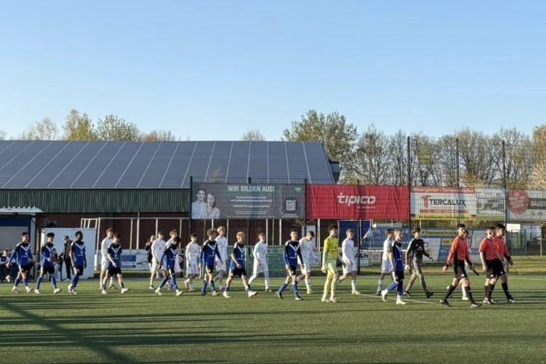 Spieler in blauen und weißen Trikots betreten das Fußballfeld, begleitet von Schiedsrichtern in Schwarz.