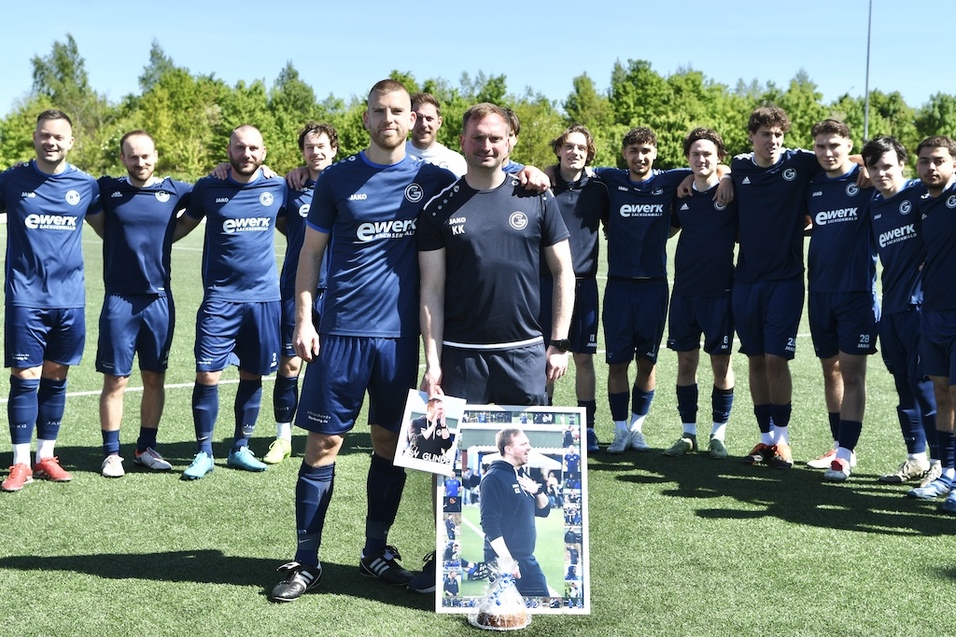 Gruppensfoto einer Fu&szlig;ballmannschaft auf einem Kunstrasenplatz, dabei zwei Spieler mit einem gerahmten Bild.