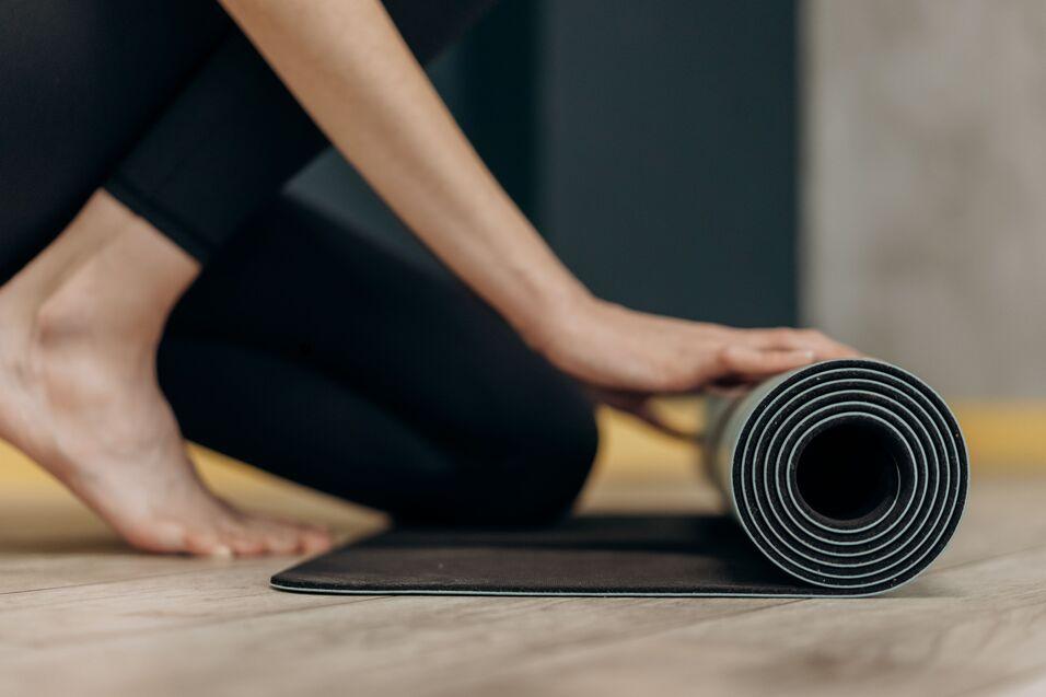 Nahaufnahme einer Person, die eine schwarze Yogamatte auf einem Holzboden aufrollt.