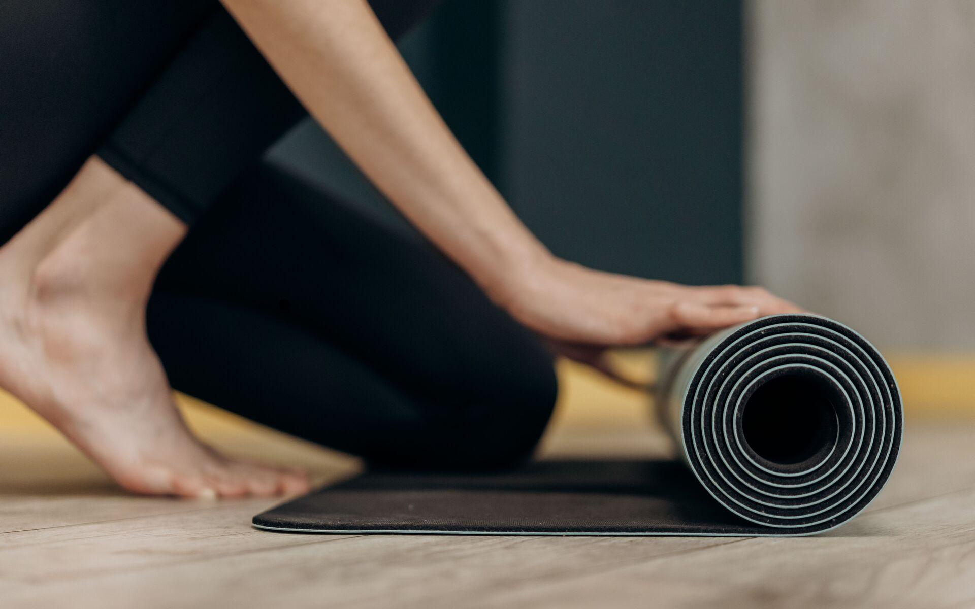 Nahaufnahme einer Person, die eine schwarze Yogamatte auf einem Holzboden aufrollt.
