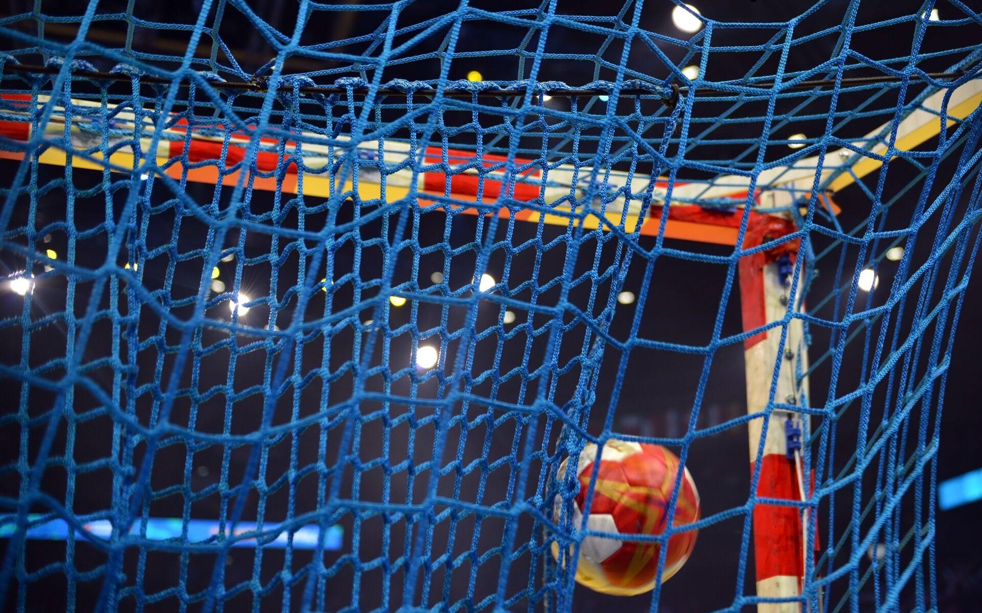 Nahaufnahme eines Handballs, der ins Tornetz eines Handballziels fliegt, mit blauer Netzstruktur im Hintergrund.