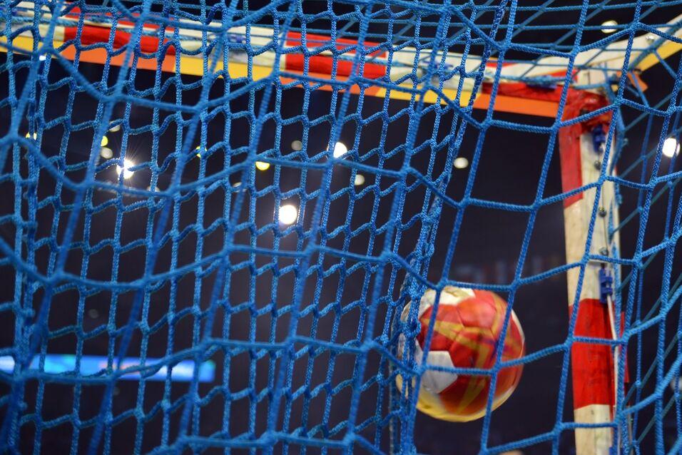 Nahaufnahme eines Handballs, der ins Tornetz eines Handballziels fliegt, mit blauer Netzstruktur im Hintergrund.