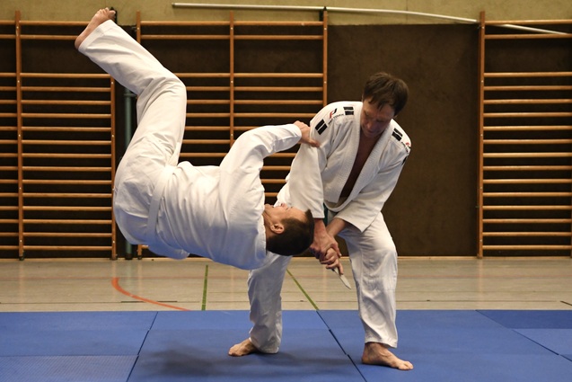 Zwei Judokas f&uuml;hren eine Technik auf einer blauen Matte in einer Sporthalle aus.