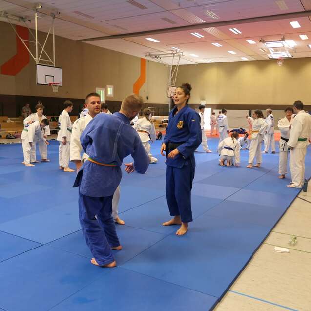 Judo-Training in Sporthalle mit mehreren Kämpfern auf blauen Matten, zwei Athleten unterhalten sich im Vordergrund.