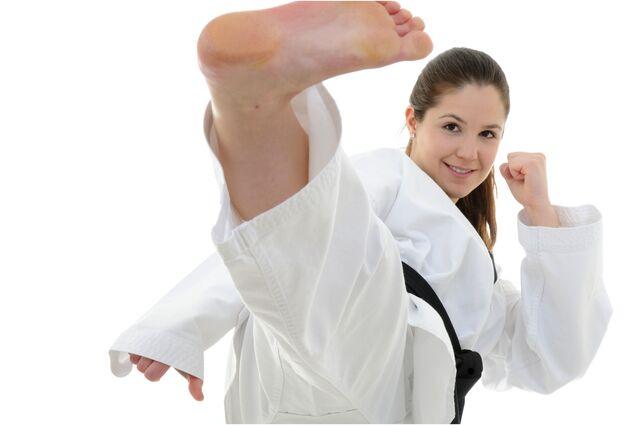 Junge Frau in Karate-Uniform führt einen Fußtritt aus, mit fokussiertem Gesichtsausdruck und hochgestelltem Bein.