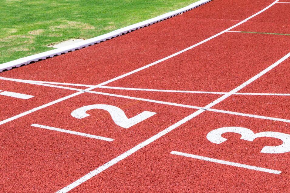 Nahaufnahme einer Laufbahn mit rot gefärbtem Belag und weißen Zahlen 1, 2 und 3 auf den Startlinien.