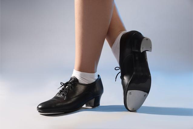 Nahaufnahme eines Fußes in einem schwarzen Stepptanzschuh mit Metallplatten, getragen mit weißen Socken.