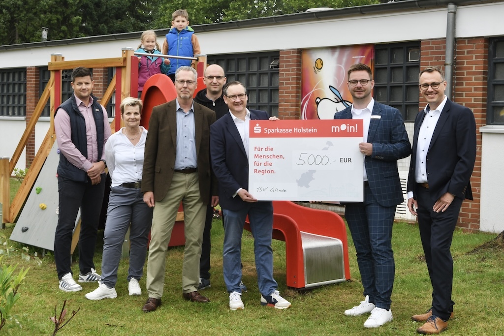 Gruppenszene mit sechs Erwachsenen und zwei Kindern, die einen gro&szlig;en Scheck &uuml;ber 5000 Euro f&uuml;r ein Projekt pr&auml;sentieren.