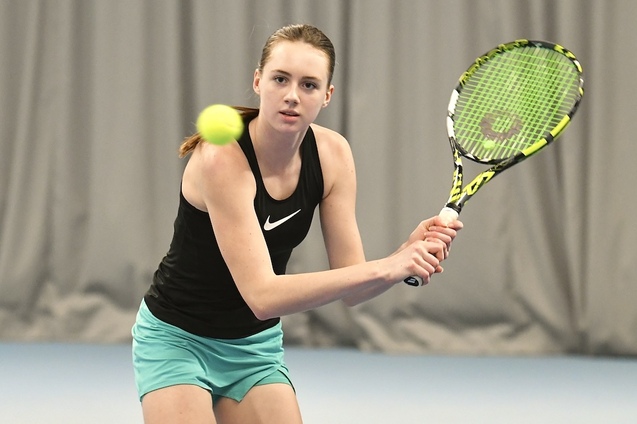 Junge Tennisspielerin schl&auml;gt einen Ball mit einem Schl&auml;ger in einer Indoor-Tennishalle.