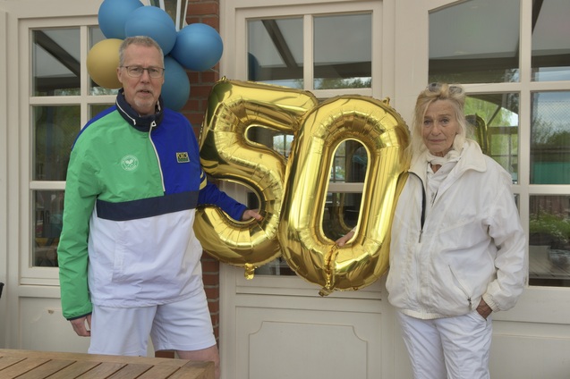 Zwei Personen halten eine goldene &bdquo;50&ldquo;-Balloon vor einem Fenster, umgeben von bunten Luftballons.