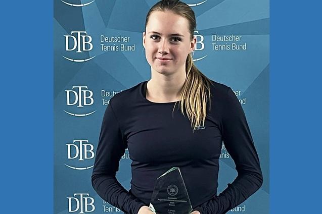 Junge Frau in sportlicher Kleidung h&auml;lt einen Pokal vor einem Hintergrund mit dem Logo des Deutschen Tennis Bundes.