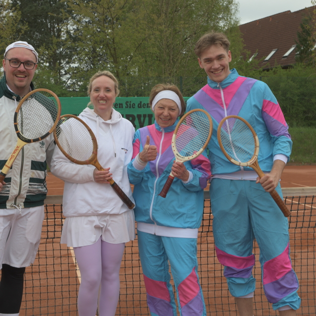 Vier Personen in sportlicher Kleidung halten Tennis-Schl&auml;ger auf einem Tennisplatz mit Sandbelag.