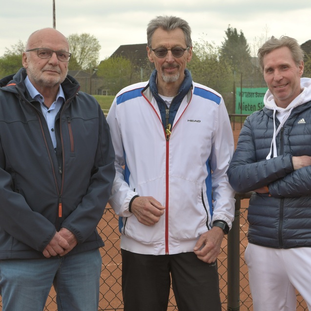 Drei M&auml;nner stehen l&auml;ssig vor einem Tennisplatz, im Hintergrund sind B&auml;ume und eine Tennisanlage sichtbar.