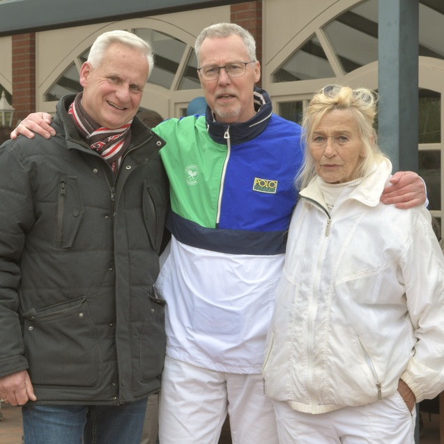 Drei Personen stehen l&auml;chelnd zusammen, eine Frau in wei&szlig;er Sportkleidung, zwei M&auml;nner, einer davon in einer bunten Jacke.