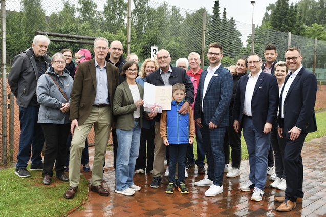 Gruppe von Menschen steht auf einem Tennisplatz, h&auml;lt eine Urkunde und posiert gemeinsam f&uuml;r ein Foto.