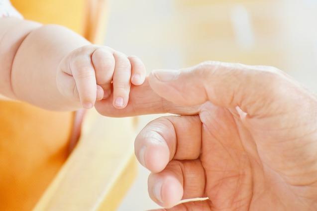 Nahaufnahme einer Babyhand, die sanft einen Finger eines Erwachsenen ber&uuml;hrt. Heller Hintergrund.
