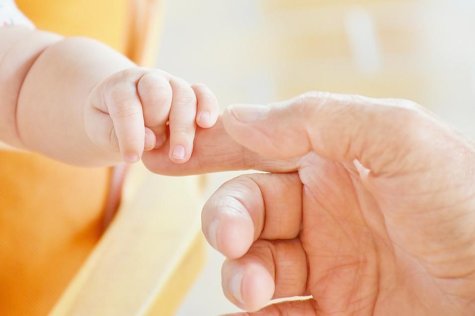 Nahaufnahme einer Babyhand, die sanft einen Finger eines Erwachsenen ber&uuml;hrt. Heller Hintergrund.