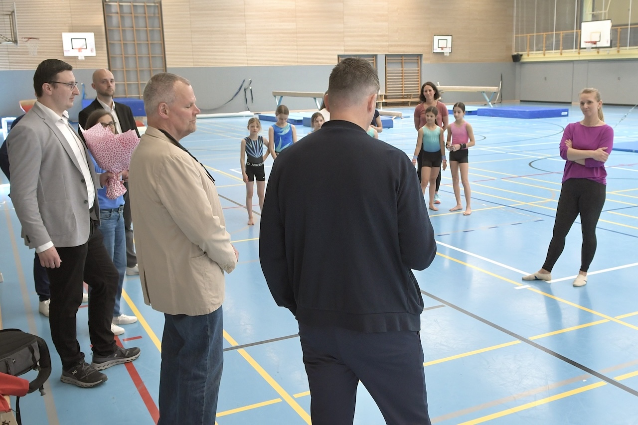 Gruppe von Erwachsenen und Kindern in einer Sporthalle, w&auml;hrend einer &Uuml;bungsbesprechung f&uuml;r Gymnastik.
