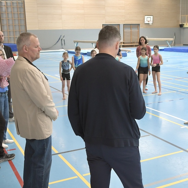 Gruppe von Erwachsenen und Kindern in einer Sporthalle, w&auml;hrend einer &Uuml;bungsbesprechung f&uuml;r Gymnastik.