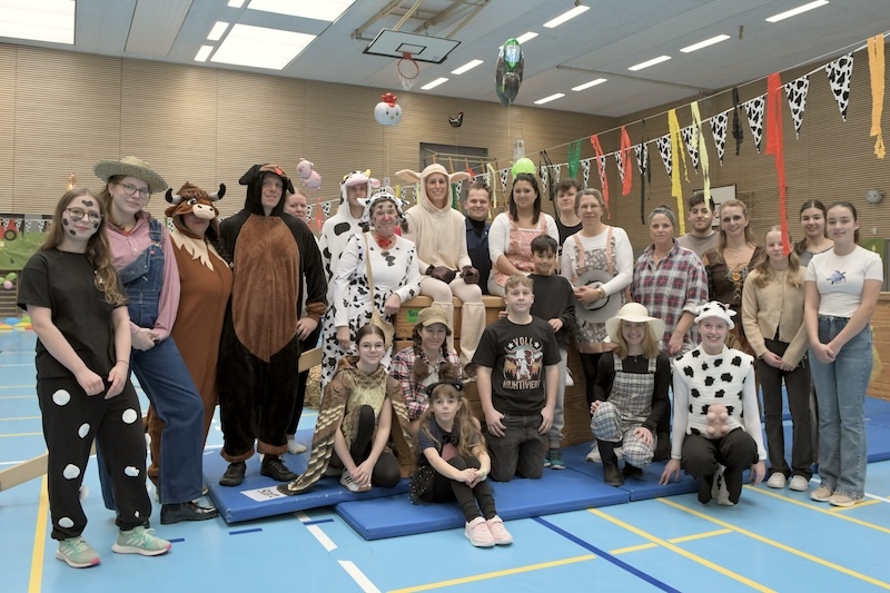 Gruppe von Menschen in Tierkost&uuml;men, posierend in einer Sporthalle mit bunten Dekorationen und Feststimmung.