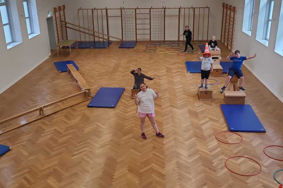 Kinder trainieren in einer Sporthalle mit Matten, Bänken und Geräten zur Förderung der motorischen Fähigkeiten.