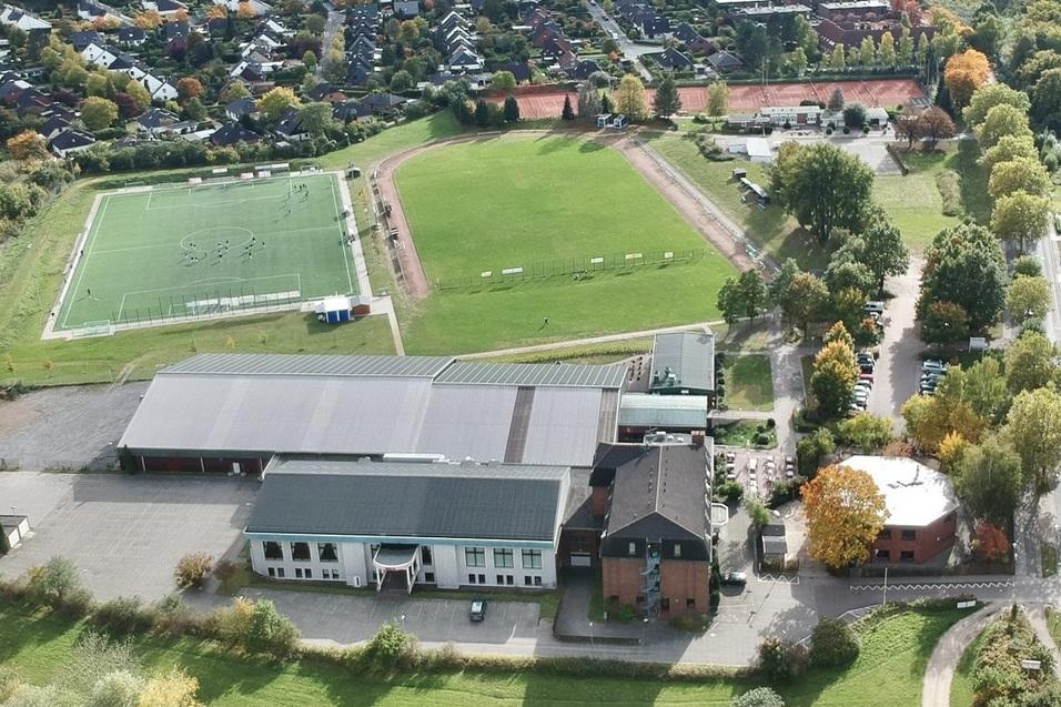 Luftaufnahme eines Schulgel&auml;ndes mit Sportpl&auml;tzen, einem Schulgeb&auml;ude und umliegenden Wohngebieten.