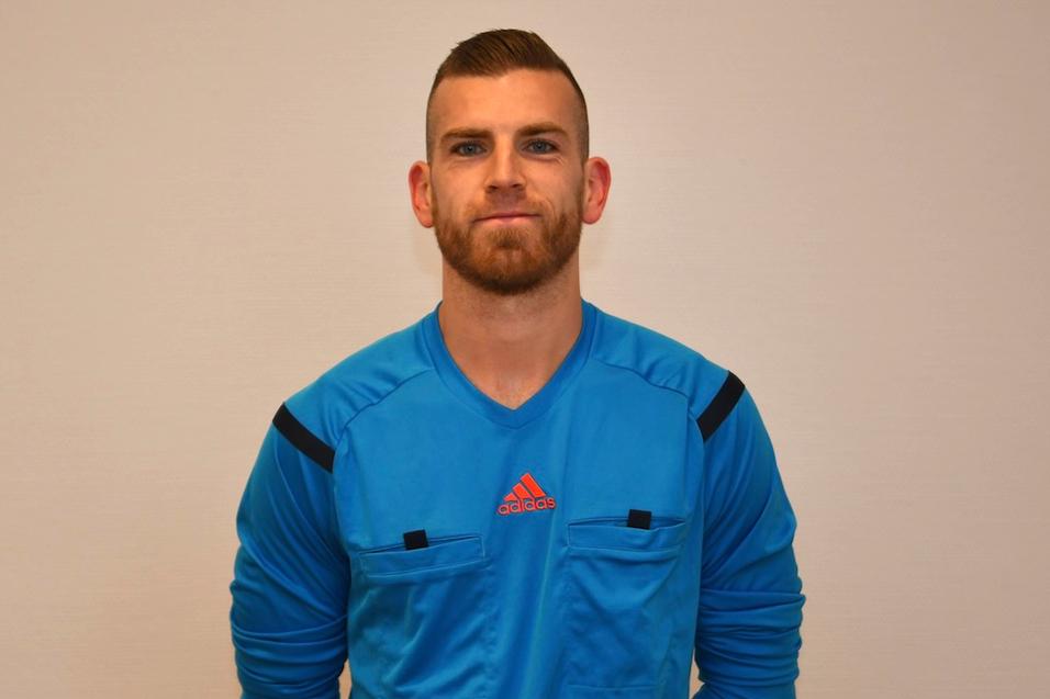 Portrait eines Mannes in blauer Sportbekleidung mit kurzen &Auml;rmeln, l&auml;chelnd vor neutralem Hintergrund.