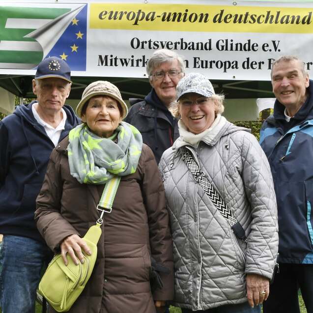 Fünf Personen stehen lächelnd vor einem Zeltdach mit dem Banner „europa-union deutschland“ in einem Park.