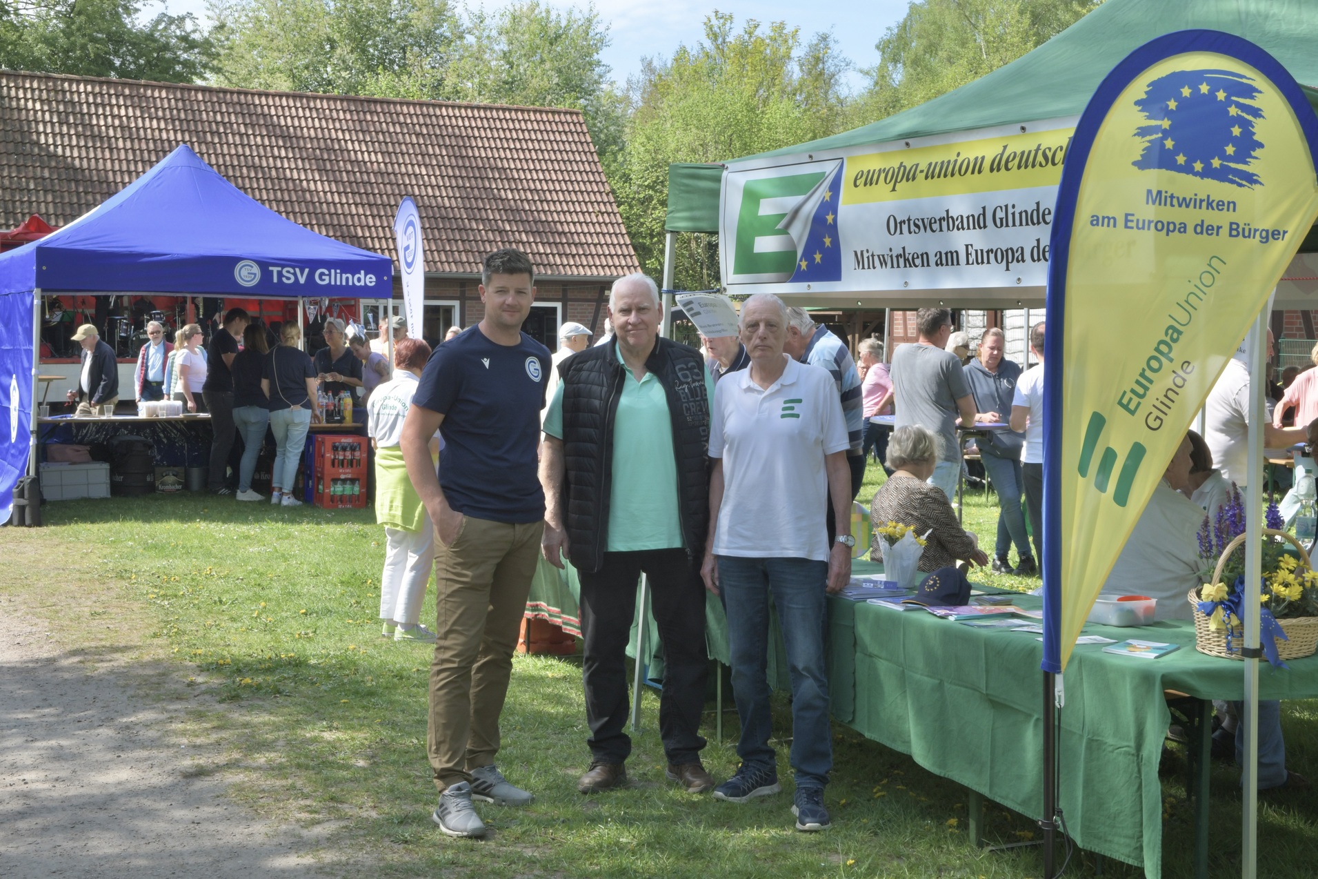 Drei M&auml;nner stehen vor einem Stand der Europa-Union auf einer Veranstaltung im Freien, umgeben von Besuchern und Zelten.