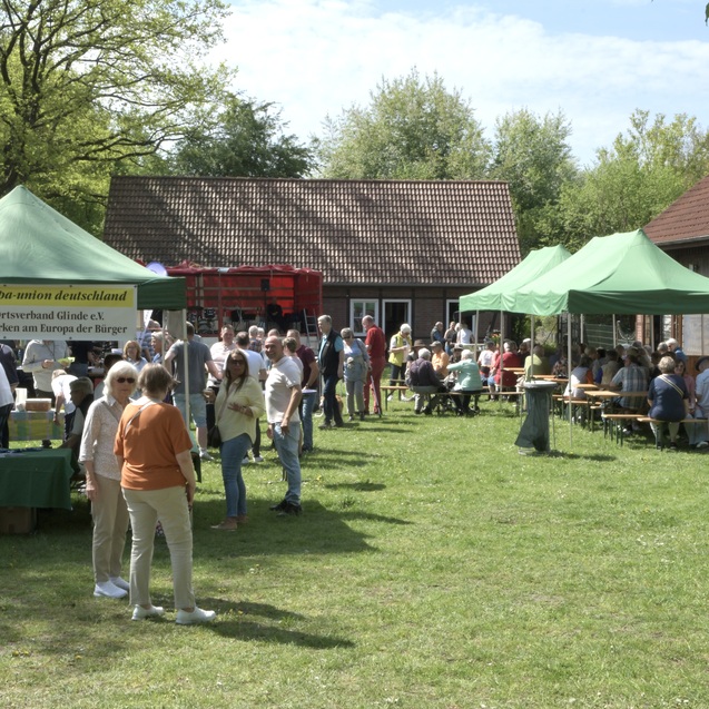 Menschenmenge auf einer Wiese mit mehreren gr&uuml;nen Zelten und St&auml;nden neben einem Bauernhaus.