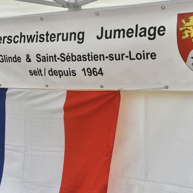 Banner mit der Aufschrift &bdquo;Verschwisterung Jumelage Glinde & Saint-S&eacute;bastien-sur-Loire seit 1964&ldquo; und Flaggen.