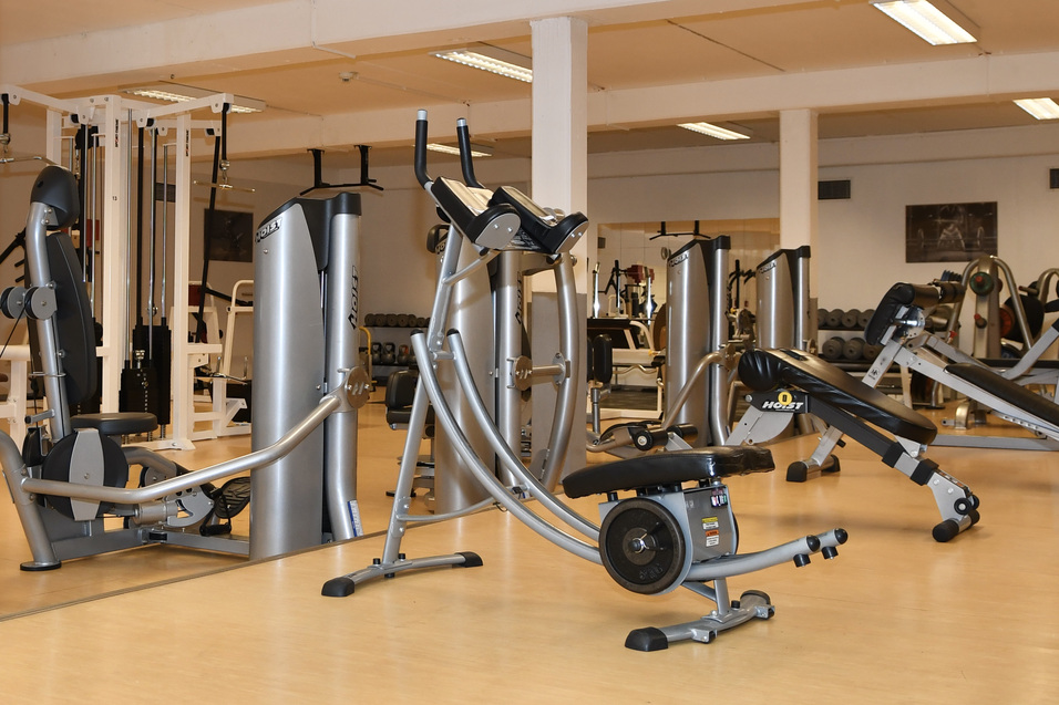 Fitnessstudio mit verschiedenen Trainingsger&auml;ten, darunter Laufband, Fahrradergometer und Kraftstationen in heller Umgebung.